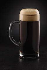 Stein with fresh stout beer with cap of foam on a black.
