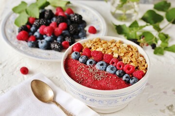 Colorful raspberry smoothie bowl with granola and fresh fruit, chia seeds. Breakfast berry smoothie bowl topped with blueberries, raspberry, blackberry, chia seeds, oat flakes and muesli.