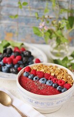 Colorful raspberry smoothie bowl with granola and fresh fruit, chia seeds. Breakfast berry smoothie bowl topped with blueberries, raspberry, blackberry, chia seeds, oat flakes and muesli.