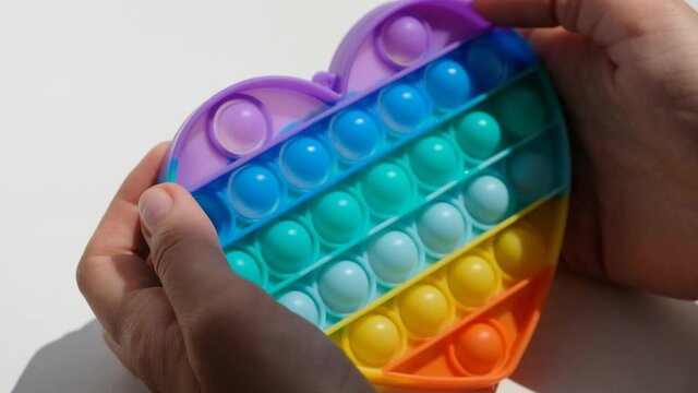 Hands play with antistress pop it toy. Rainbow sensory fidget isolated on white background. New trendy silicone toy.