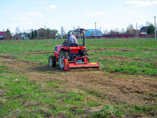 Obraz premium a man rides a tractor with a mower in a field. Mulching and mowing the grass. Clear day, blue sky. Land cultivation