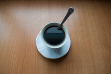 Taza blanca de café negro con cucharita sobre mesa de madera clara vista desde arriba