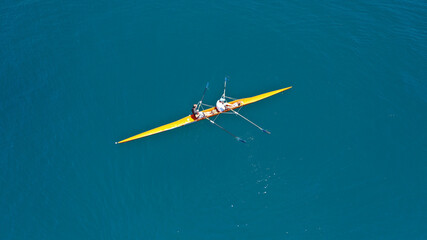 Aerial drone top down view of sport canoe operated by team of young trained athletes in deep blue...