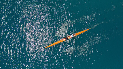 Aerial drone top down view of sport canoe operated by team of young trained athletes in deep blue...