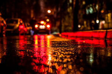 Obraz premium Rainy night in the big city, alley between houses with a car traveling. View from the level of asphalt
