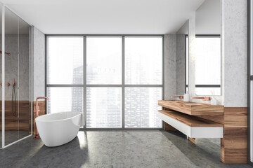 Modern design bathroom interior with shower cabin, white oval bathtub, double sink countertop, bronze faucets. Panoramic window with skyscrapers city view. Wood and concrete materials.
