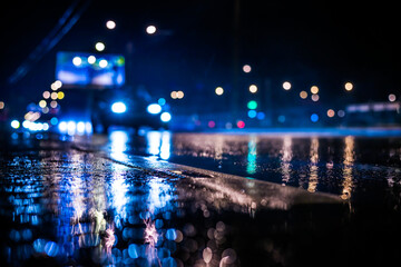 Rainy night in the big city, the light from the headlamps of approaching car on the highway. View from the level of the dividing line