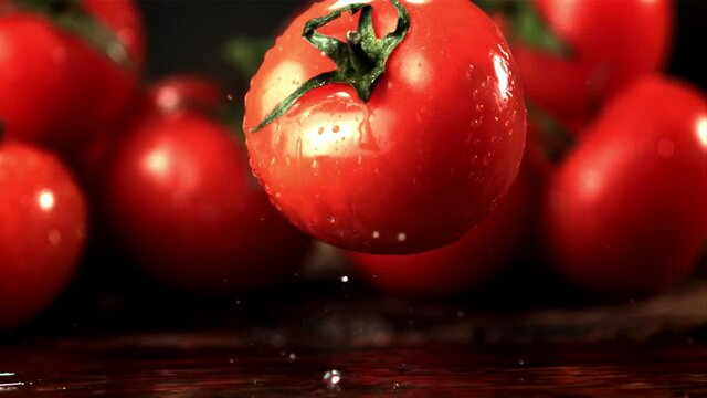 Super slow motion fresh tomato falls on the table with splashes of water. Filmed at 1000 fps.On a wooden background.