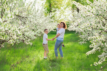 Obraz premium rear view.mother with sons walks in flowering garden. youngest child in her arms
