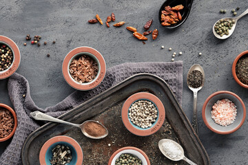 Obraz na płótnie Canvas Various spices in ceramic oriental spoons and pinch bowls on dark vintage metal tray. Textile towel on dark textured wood background. Flat lay, top view. Dry herbs, pepper, salt, crispy chili, thyme.
