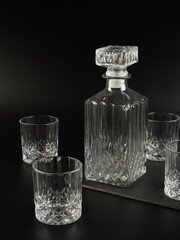 Empty decanter and four empty whiskey glasses on dark background