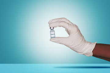 Hand with glove holds a Corona virus ampoule against a blue background