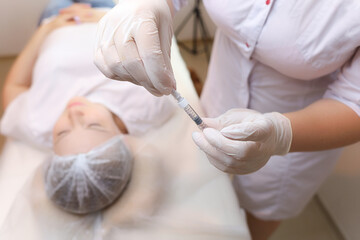 The cosmetologist holds the filler for injections of hyaluronic acid and removes the protective cap from the needle
