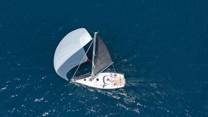 Aerial drone top down photo of beautiful sail boat with trained crew cruising in deep blue Aegean sea