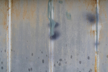 The wall is made of gray metal panels. There are vertical joints, slight corrosion, darker paint stains. At the bottom of the Windows there are traces of water or oil drops. Background. Texture.