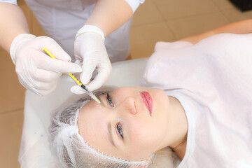 A cosmetologist performs a facial rejuvenation procedure by injecting injections to smooth out wrinkles in the forehead area