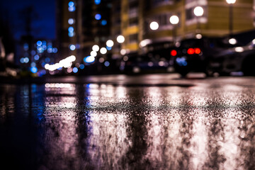 Rainy night in the big city, the light from the lanterns in the courtyard of the house in which the parked cars. View from the level of asphalt