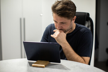 Focused unshaven handsome guy looking tablet, working from home remotely, participating in online...
