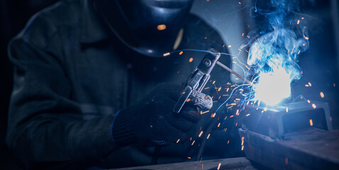 Professional welder performs work with metal parts in factory, sparks and electricity. Industry worker banner