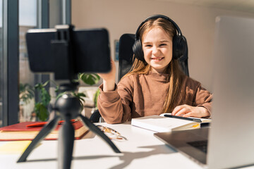 Little schoolgirl in headphones is engaged in distance learning at the computer