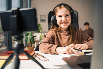 Little schoolgirl in headphones is engaged in distance learning at the computer