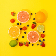 Citrus fruit, strawberries and blueberries arranged on yellow background. Flat lay concept.