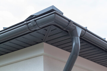 Corner of house with new gray metal tile roof and rain gutter. Metallic Guttering System, Guttering...