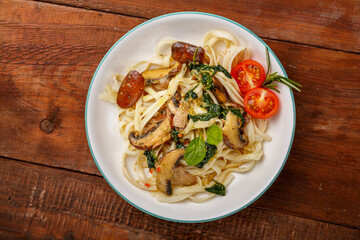 Udon with mushrooms and spinach and cherry tomatoes in a plate on a wooden table.