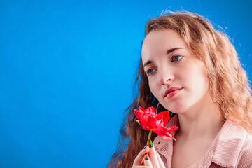 Obraz na płótnie Canvas Romantic beautiful pensive girl with long wavy hair holding red tulip