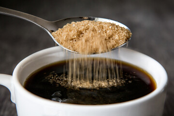 Raw sugar being put into a cup of coffee 