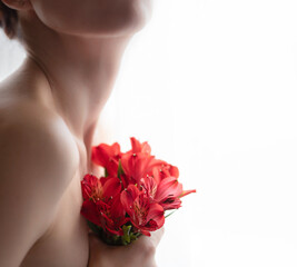 A naked girl in defocus holds a bouquet of red alstroemeria. Front view. Selective focus. 