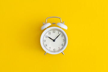 White antique alarm clock on yellow background. Flat lay composition. Top view.