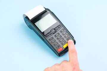 Man hand pushing a button on POS terminal with roll paper cash tape on the blue background