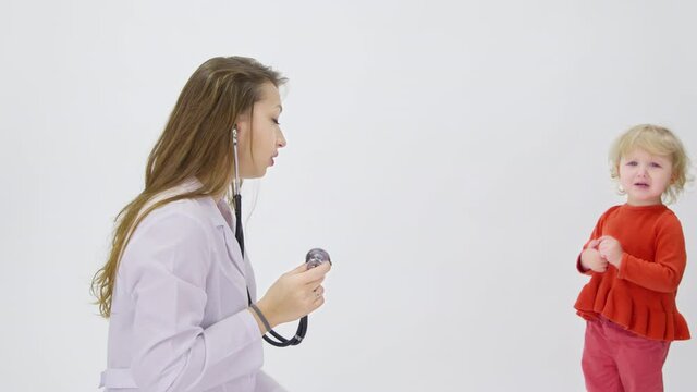 Adorable cranky tired sleepy toddler girl Does not let doctor listen to lungs with stethoscope isolated on white. child visits pediatrician, children's health. Infantile caprices, tantrums concept