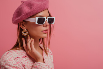 Elegant fashion model wearing classic beret, stylish rectangle white frame sunglasses, trendy pearl earrings, posing on pink background. Copy, empty space for text 