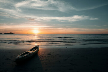 A kayak lies on the beach during a beautiful sunset.