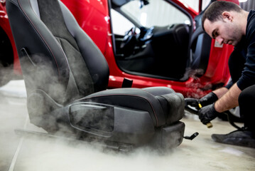 Car service worker cleaning car seat with a steam cleaner