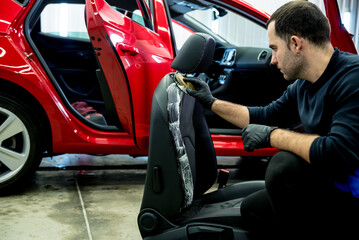Car service worker cleans a car seat with a special brush