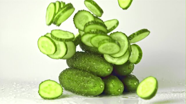 Super slow motion pieces of cucumber fall on a bunch of cucumbers on the table. On a white background. Filmed on a high-speed camera at 1000 fps. High quality FullHD footage