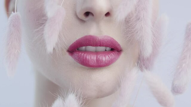 Female lips close up. Pink lipstick. Decorative flowers. Woman face with clean skin on a pink background. Clean face skin. Skin care. Idea for advertising cosmetic products. Beauty treatments.