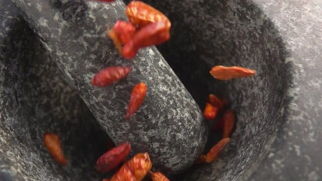 Close-up of red cayenne pepper pods falling and bouncing in the stone mortar