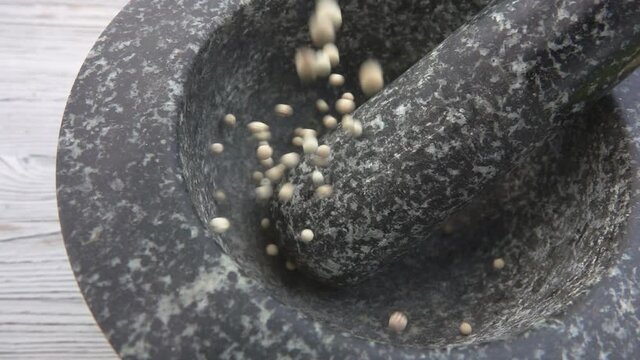 Spicy exotic white peppercorns are falling and bouncing in the grey stone mortar