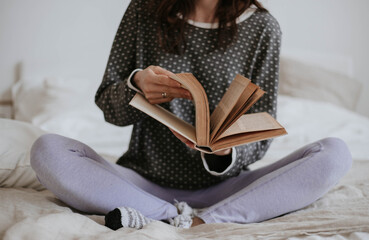 girl in cozy pajamas sitting on the bed, leafing through a vintage book
