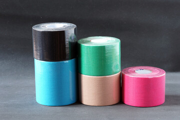 Rolls of bright, multi-colored kinesio tapes in transparent plastic packaging on a gradient gray background.