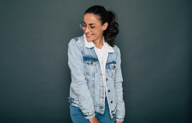 Modern trendy stylish beautiful brunette woman in denim clothes is posing on the gray background