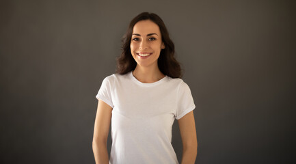 Young beautiful stylish happy woman in a white t-shirt is posing on the gray background