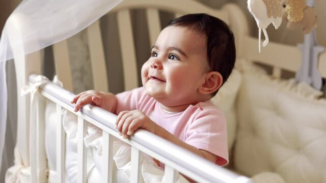 Cute baby 9 months laughing in a cot in the room of the house