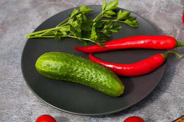Fresh homemade cucumber with red pepper and parsley on a black plate. 