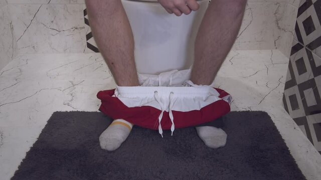 Legs of a young man in socks who came to the toilet and sits on the toilet