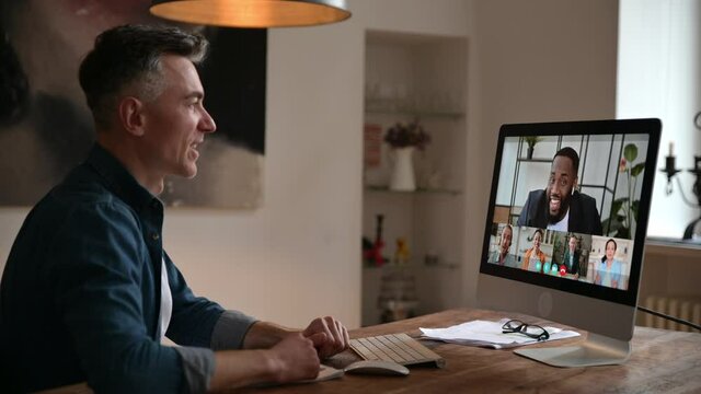 Video call concept. Side view at caucasian confident man, manager or freelancer, and at computer screen with business partners gathered in a group online conference to discuss work issues and strategy